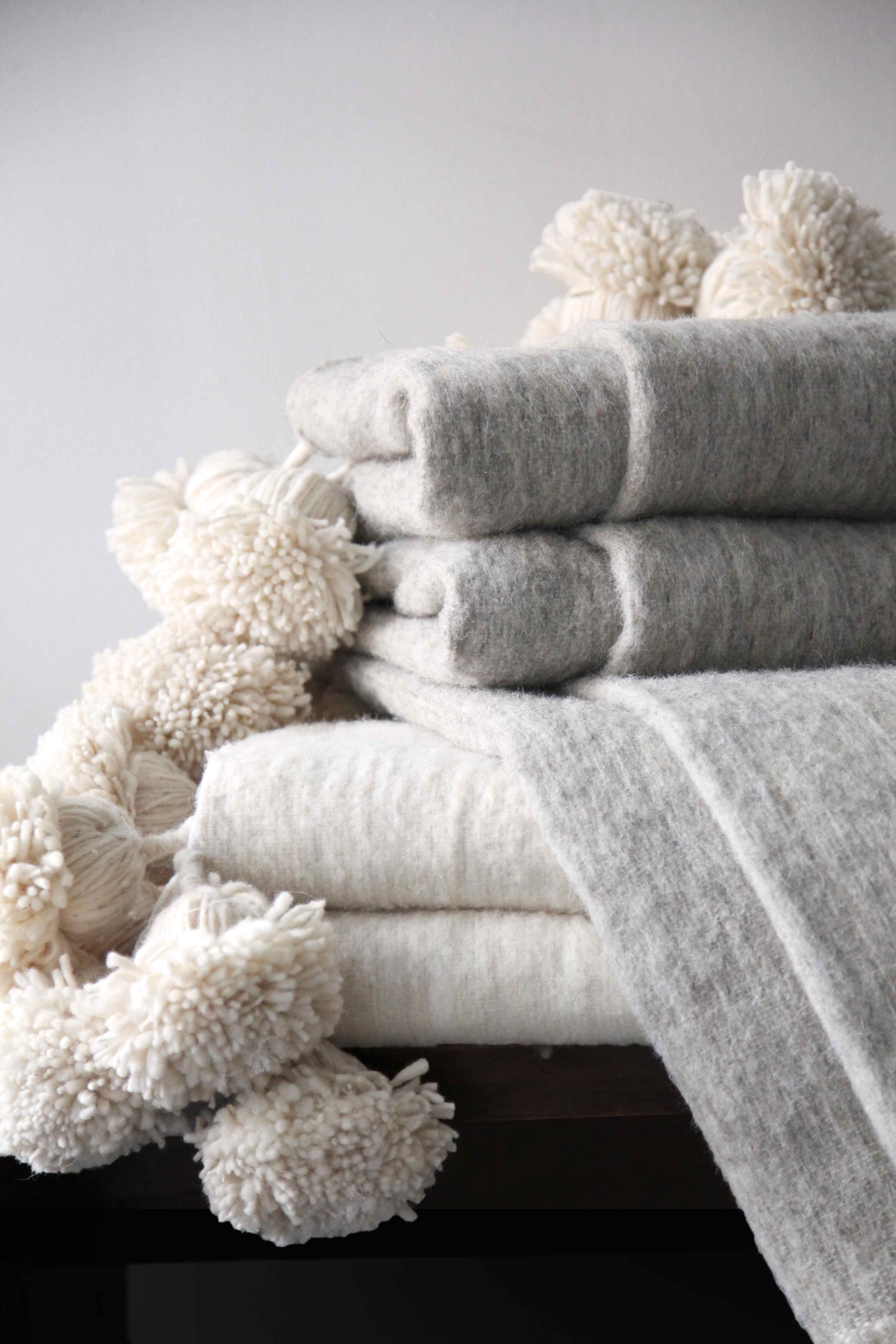 traditional moroccan thick wool pom pom blankets in solid natural dyed colors and stripes.